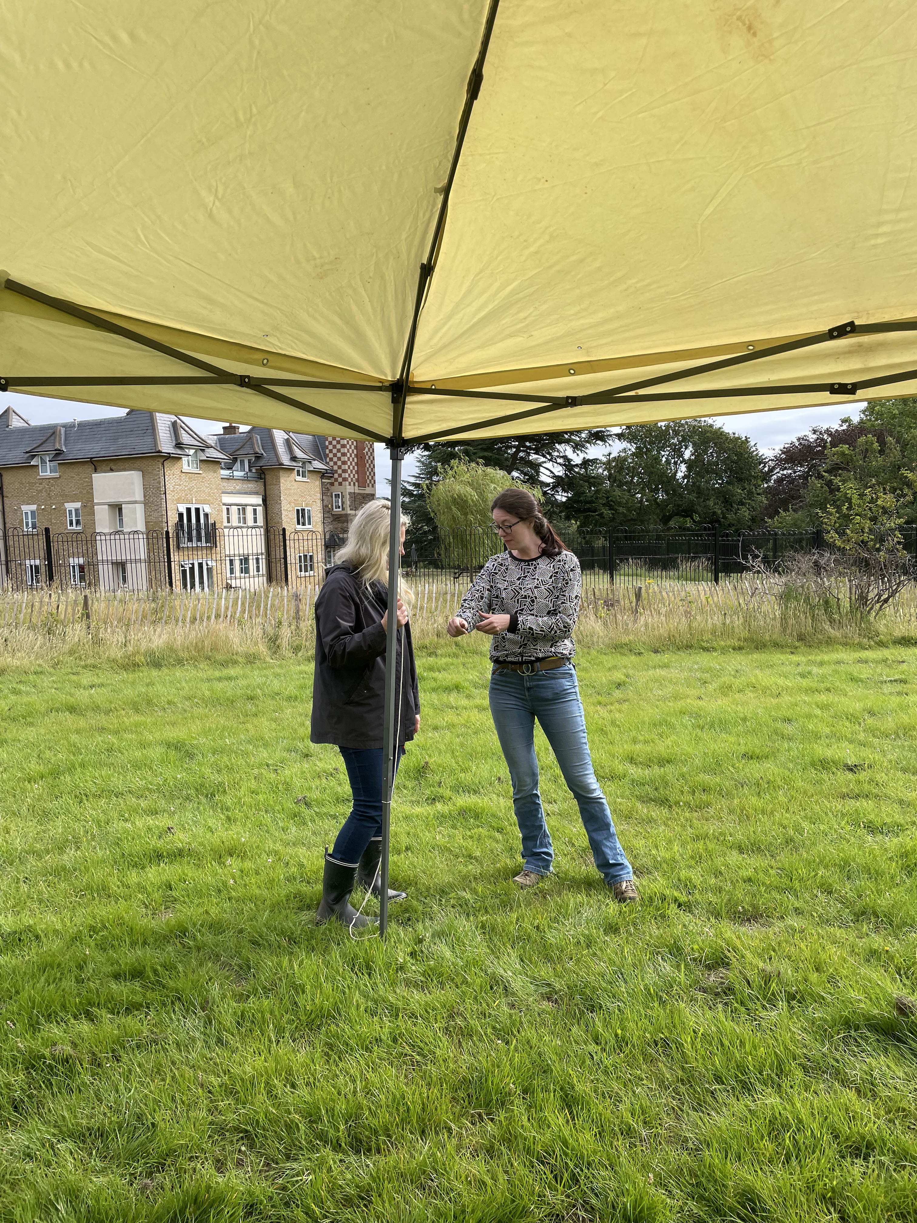 Hayley and Isabel stand under a marquee. Isabel is showing Hayley her nice black and white jumper