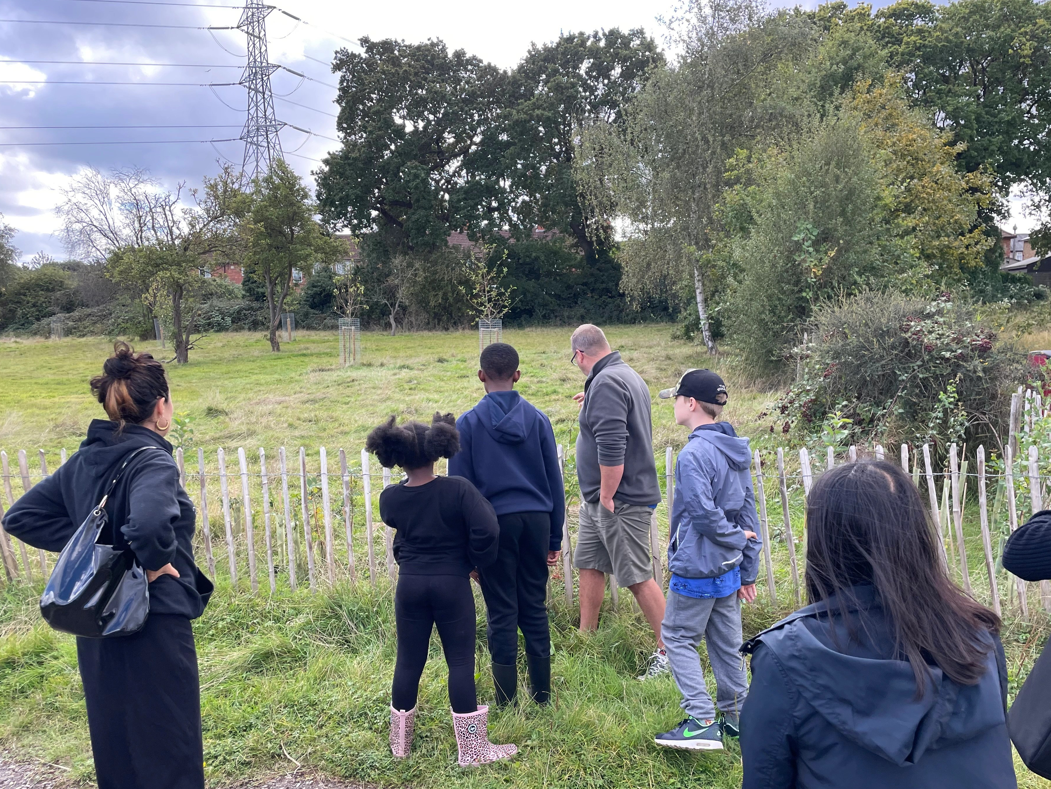 Man in shorts shows a group of people some hedgerow in Poulter Park orchard