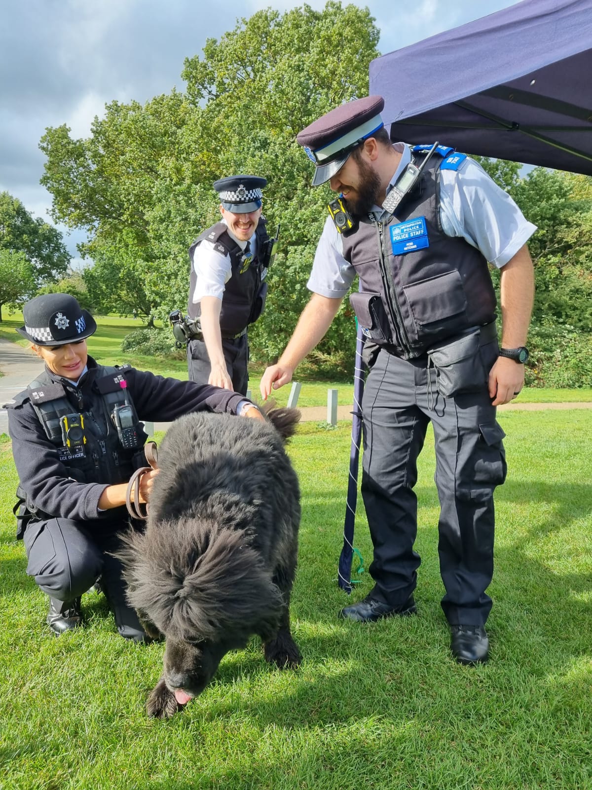 three police officers pet a large fluffy black dog