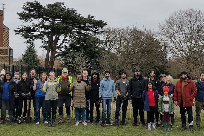 Hedgerow planting volunteers stand in front of the new hedgerow in Poulter Park with Bishopsford House chimney in the background