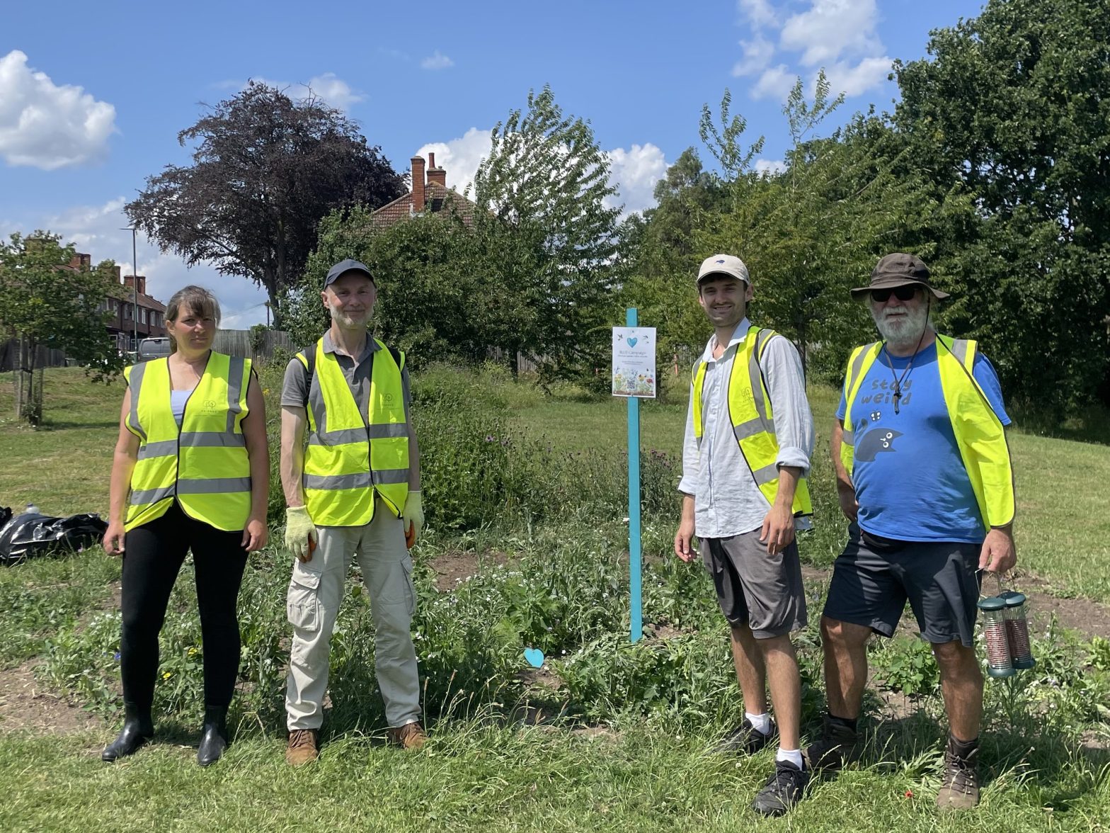 A blue signpost is planted in a flower bed. Four people in high vis stand around it