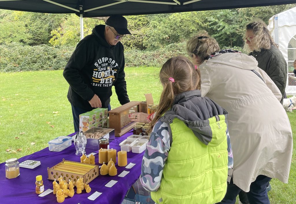 Dave stands behind a stall with candles, honey and bee hive slices talking to a group of people