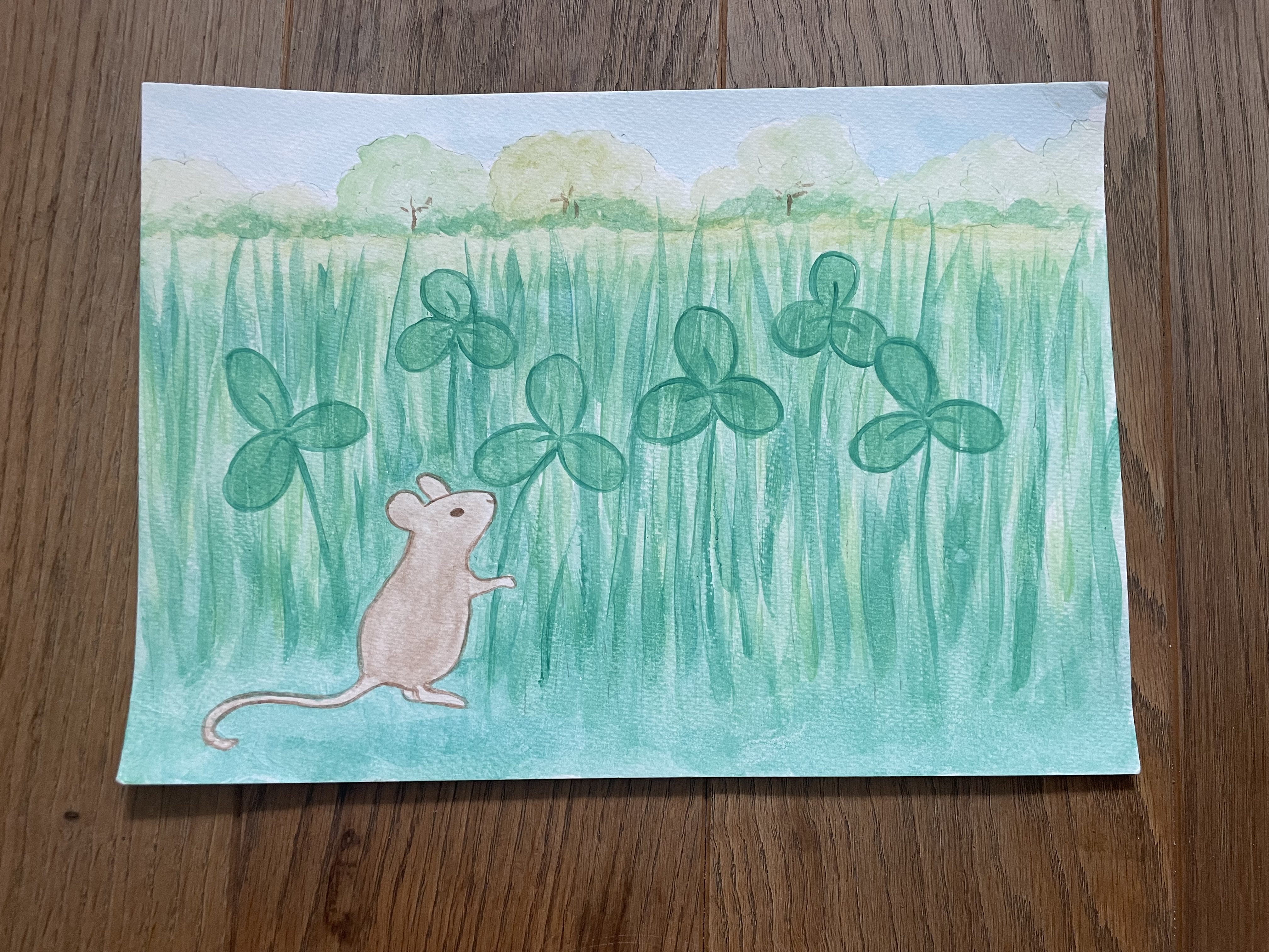 A mouse holding a clover in the foreground of a park scene with tall grass.