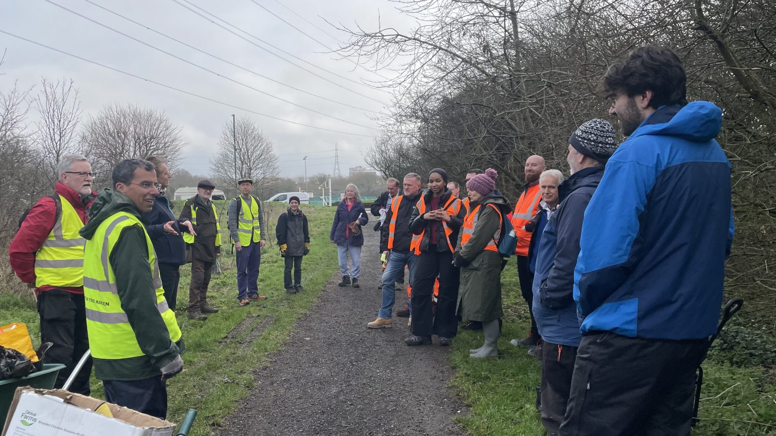 20+ people some in orange high vis being briefed on the path through Revesby Wood on a grey day.