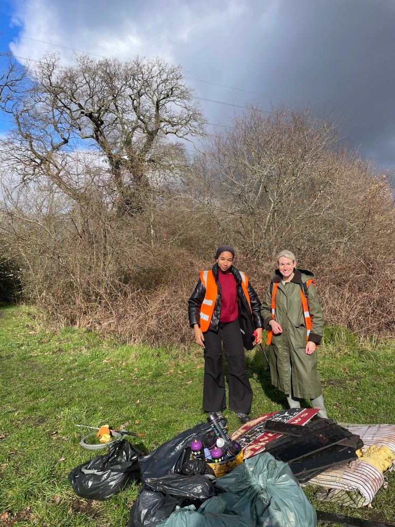 Two volunteers from Veolia stand in front of trees in Revesby Wood with a big pile of rubbish