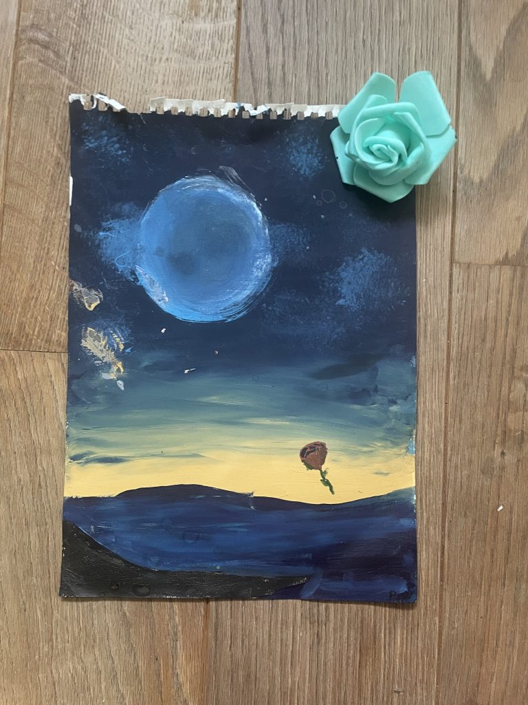 A blue sun or planet floats against a dark blue sky over an other wordly dream scape of more blues against a yellow horizon. A single red rose floats above the land, echoed by a green rose fixed to the corner of the art work.